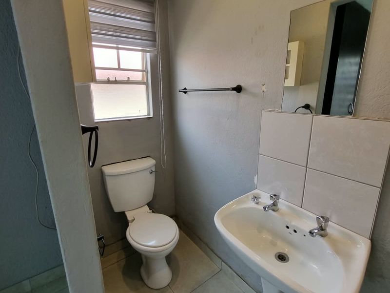 A functional bathroom featuring a pedestal basin, toilet, tiled splashback, and neutral wall finishes, providing a clean and practical space.
