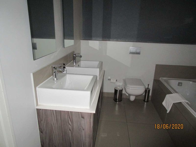 Modern bathroom featuring a double vanity with vessel sinks, a wall-mounted toilet, and a built-in bathtub with neutral tile finishes.