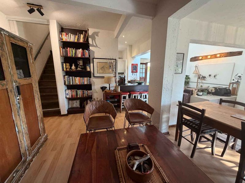 Open plan living and dining area featuring timber flooring, a built-in bookshelf, and a breakfast bar connecting to the kitchen space.