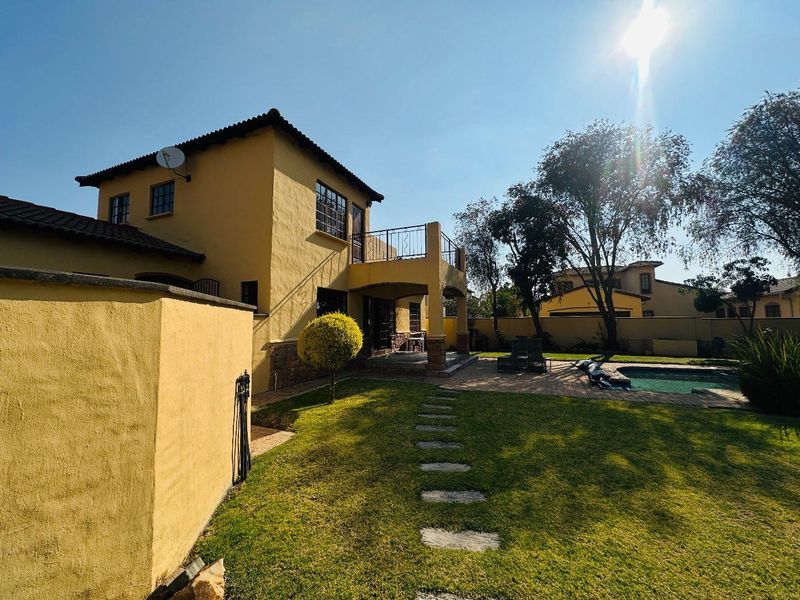 Rear view of the townhouse featuring a private garden, swimming pool, paved patio area, and an upper-level balcony with metal railings.