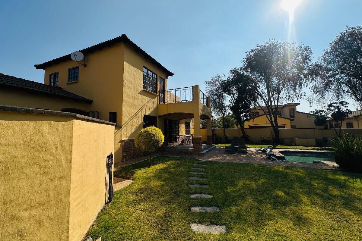 Rear view of the townhouse featuring a private garden, swimming pool, paved patio area, and an upper-level balcony with metal railings.