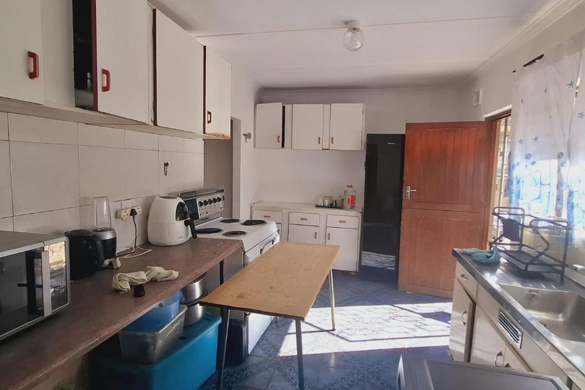 A functional kitchen featuring white cabinetry, laminate countertops, a stainless steel sink, and tiled flooring, offering potential for modernization and layout optimization.