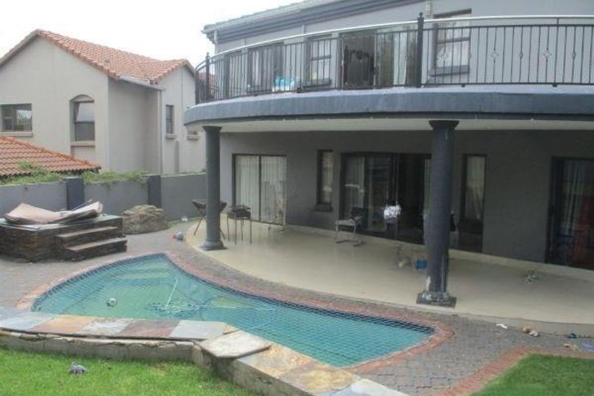 Rear exterior view featuring a covered patio, an upper-level balcony with wrought iron railings, and a swimming pool with a safety net.