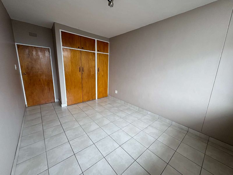 A vacant bedroom featuring neutral wall paint, tiled flooring, and built-in wooden cabinetry with overhead storage.