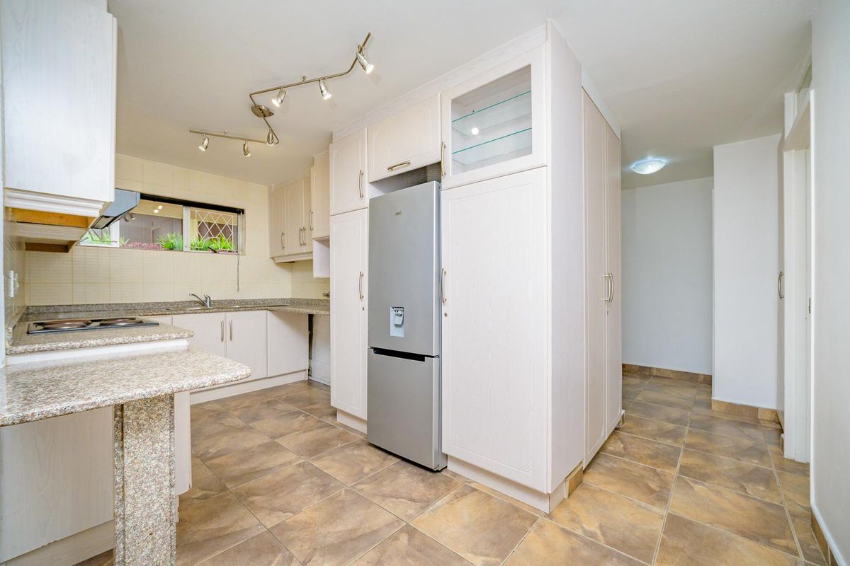 A functional kitchen featuring granite countertops, ample built-in cabinetry, a hob with extractor fan, and tiled flooring throughout.