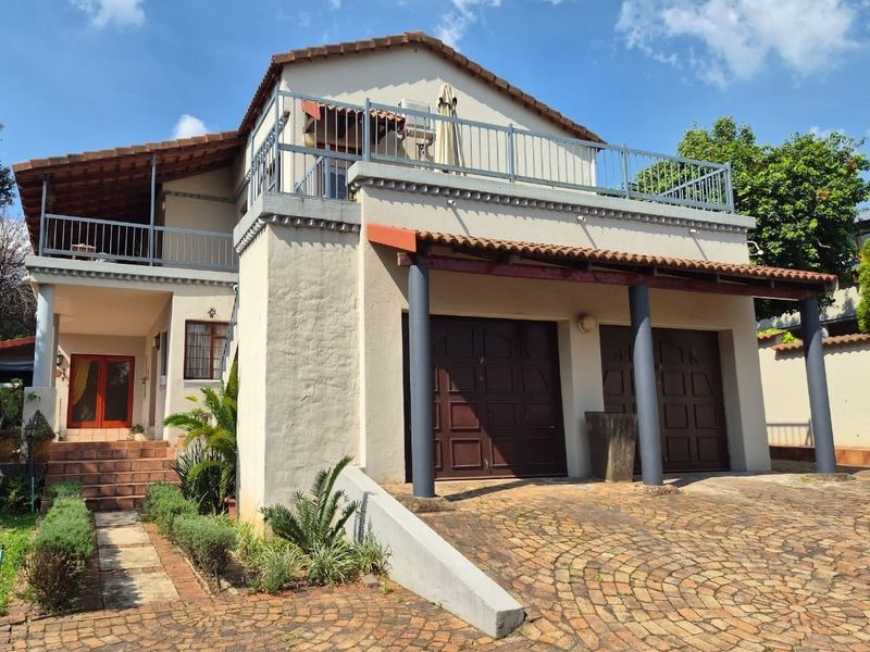 Front elevation of a multi-level house featuring a double garage, paved driveway, and an upper-level balcony with metal railings.