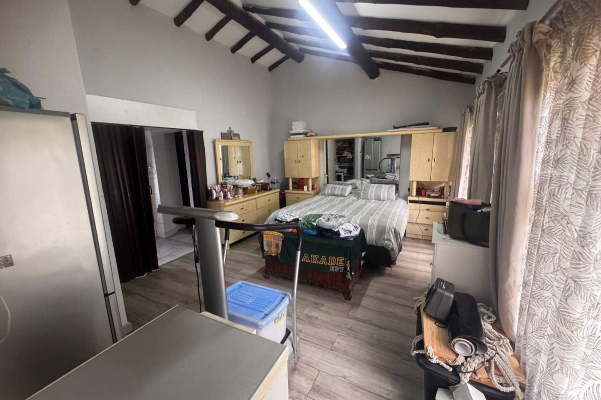 Spacious bedroom featuring exposed timber ceiling beams and laminate flooring, offering a rustic aesthetic with potential for modern updates.