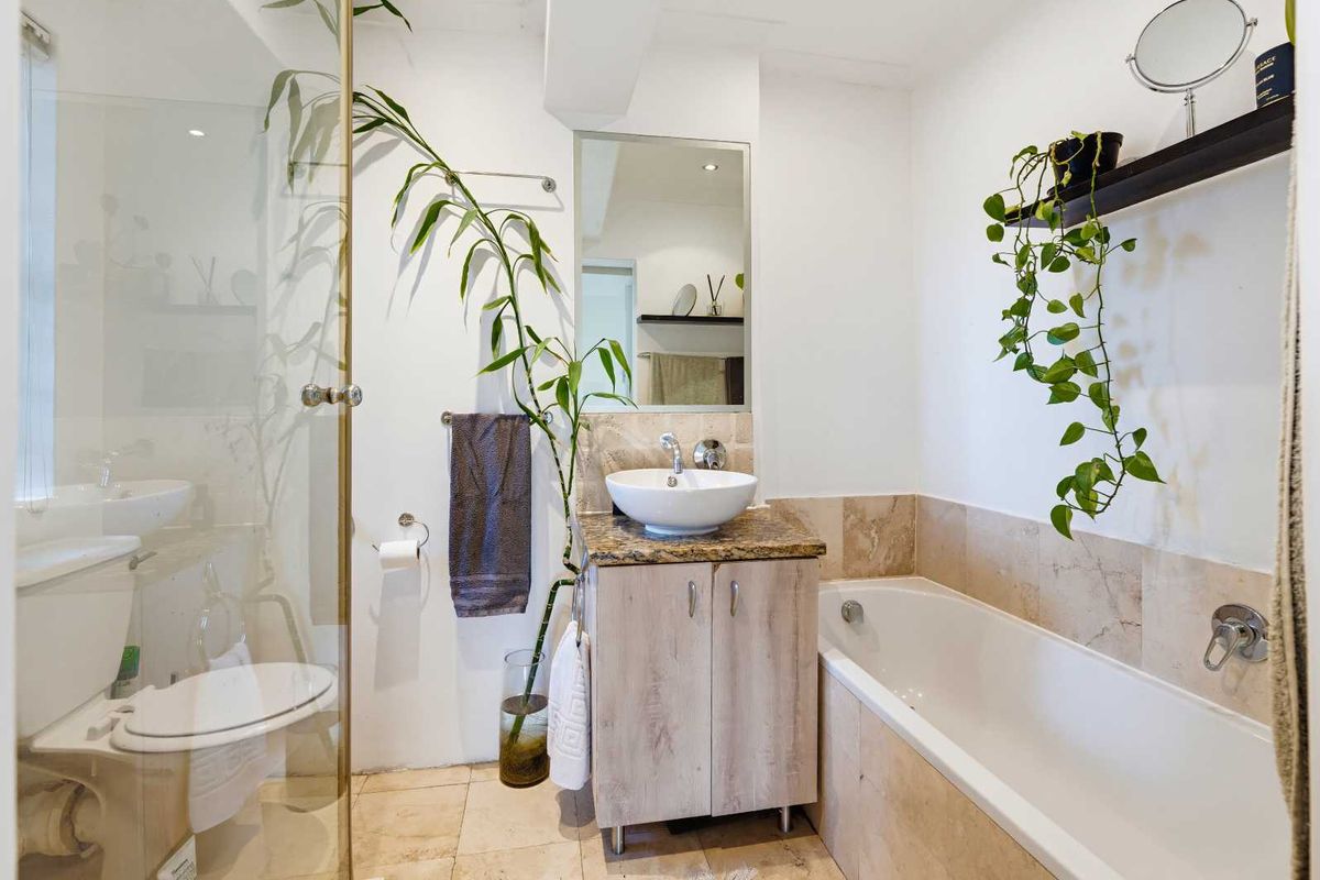 A well-appointed bathroom featuring a vessel sink on a granite vanity, a glass-enclosed shower, and a built-in bathtub with neutral travertine tiling.