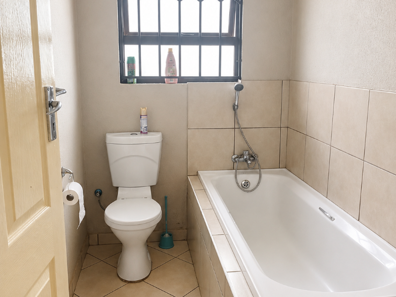 A functional bathroom featuring a built-in bathtub with a handheld shower mixer, a standard toilet, and tiled finishes throughout.