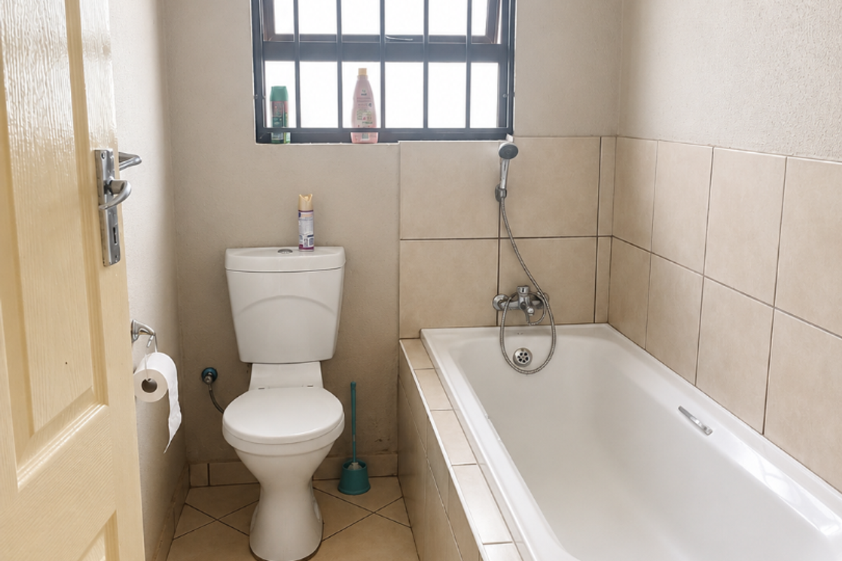 A functional bathroom featuring a built-in bathtub with a handheld shower mixer, a standard toilet, and tiled finishes throughout.