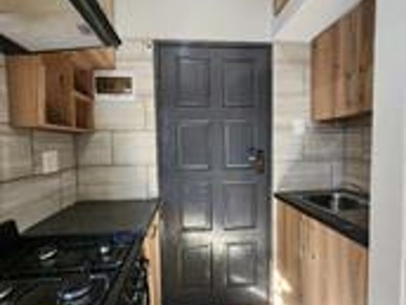 A compact kitchen featuring modern wood-finish cabinetry, dark countertops, a stainless steel sink, and tiled finishes throughout.
