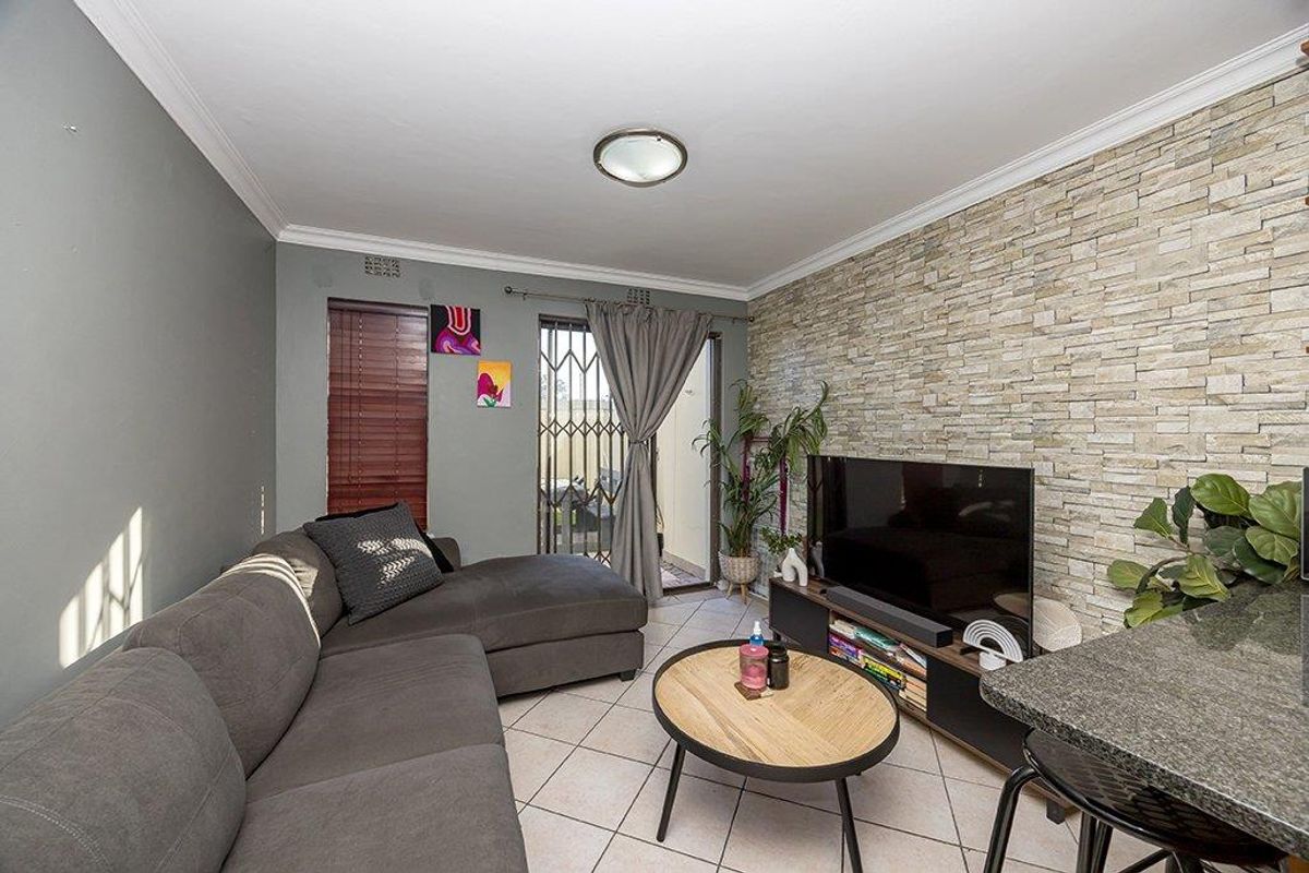 A comfortable living room featuring a textured stone veneer accent wall, ceramic tile flooring, and direct access to an outdoor area through a security gate.