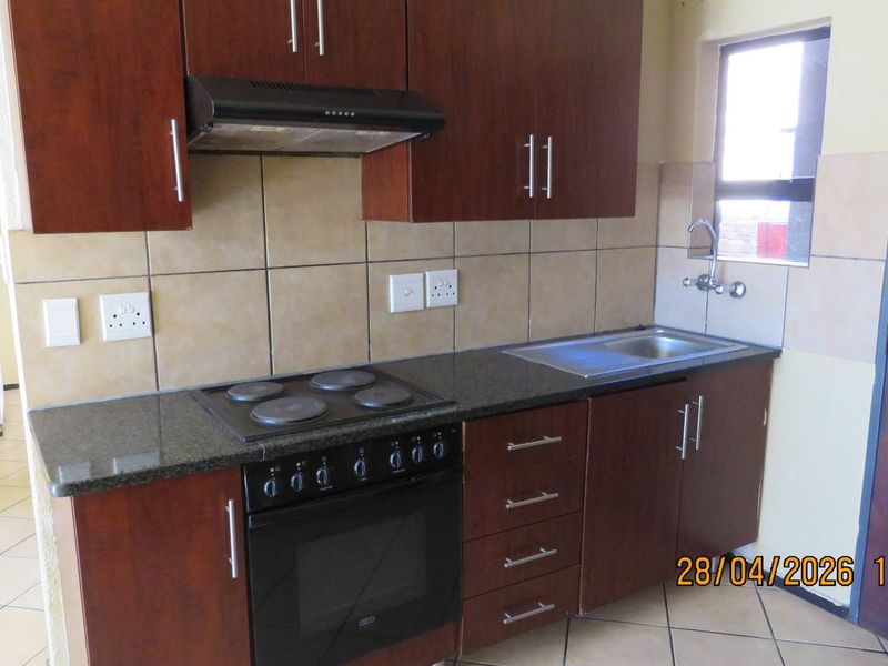 A functional kitchen featuring dark wood cabinetry, granite countertops, a built-in electric oven and hob, and tiled finishes throughout.