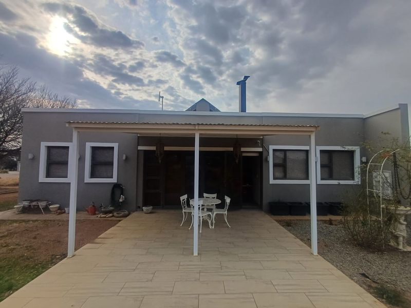 Rear view of the house featuring a covered patio area with tiled flooring, aluminium window frames, and a chimney.