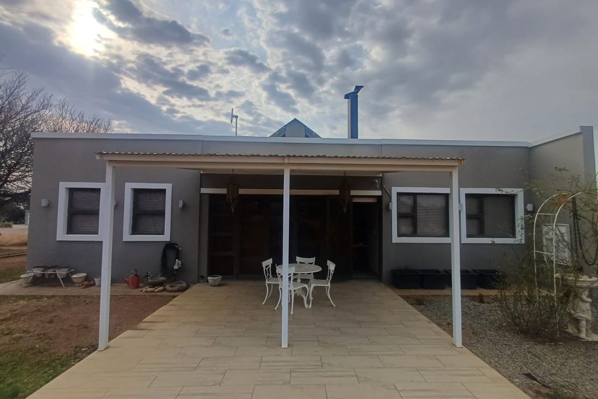 Rear view of the house featuring a covered patio area with tiled flooring, aluminium window frames, and a chimney.