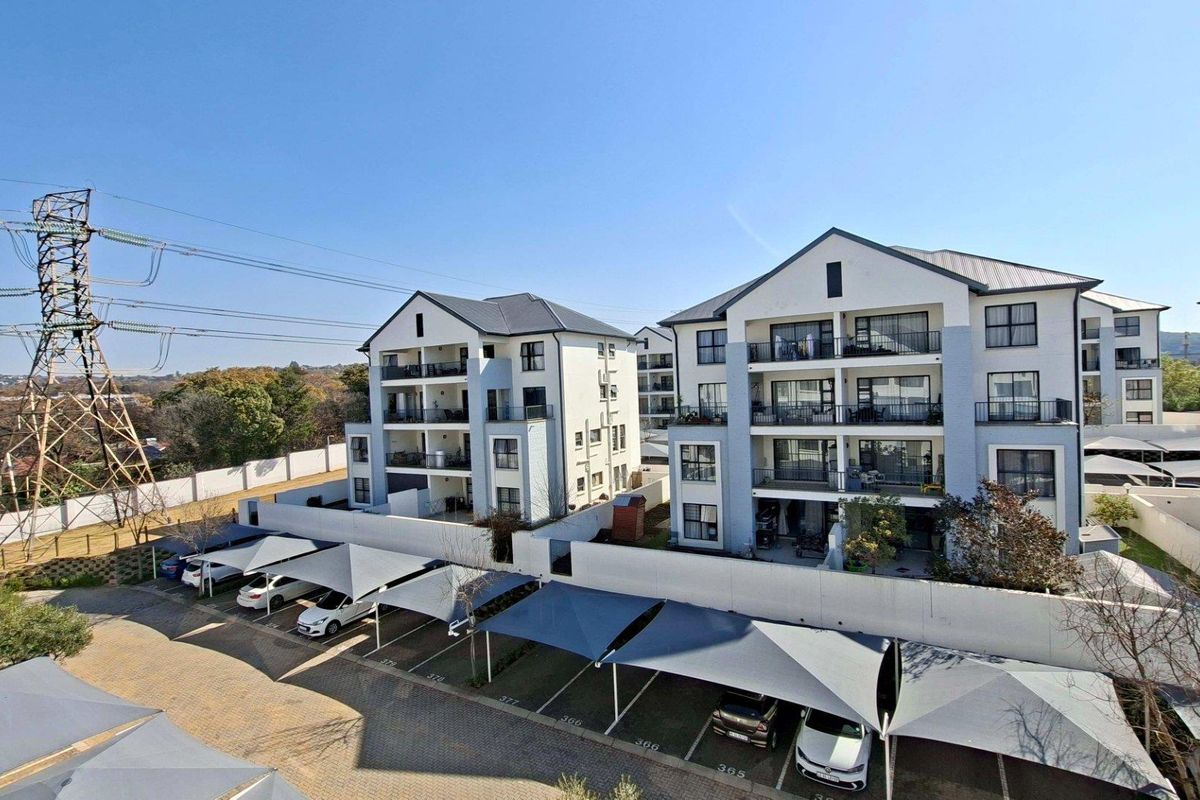 Aerial view of a modern apartment complex featuring multi-story buildings, private balconies, and designated covered parking bays within a secure perimeter.