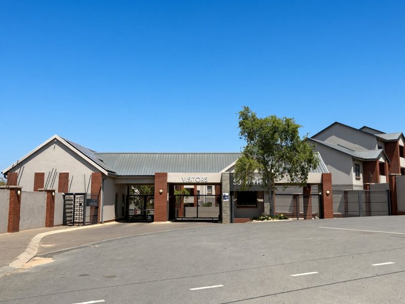 Front entrance and security gate access to Surrey Hills apartment complex, featuring brick and plaster facade with metal roofing.