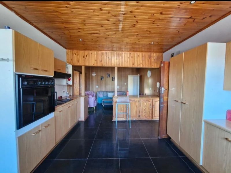 Open plan kitchen and living area featuring extensive wooden ceiling and wall paneling, dark tiled flooring, and built-in cabinetry with integrated oven.