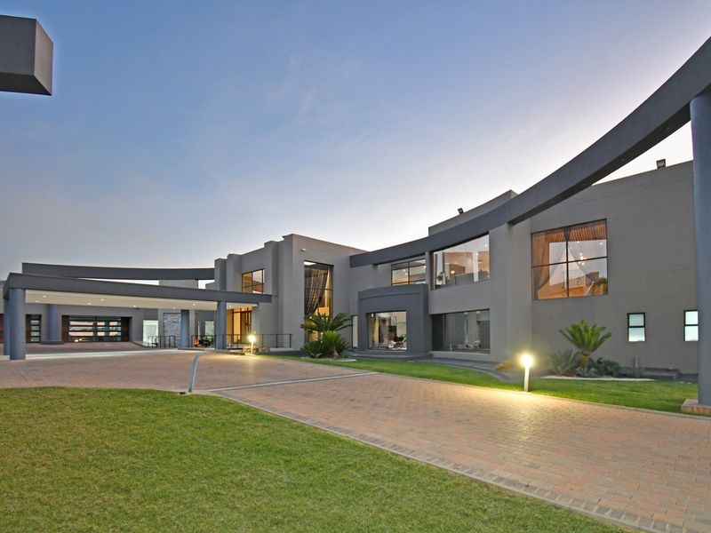 A modern, architecturally designed luxury home featuring a sweeping curved facade, expansive glass windows, and a spacious paved driveway with integrated exterior lighting.