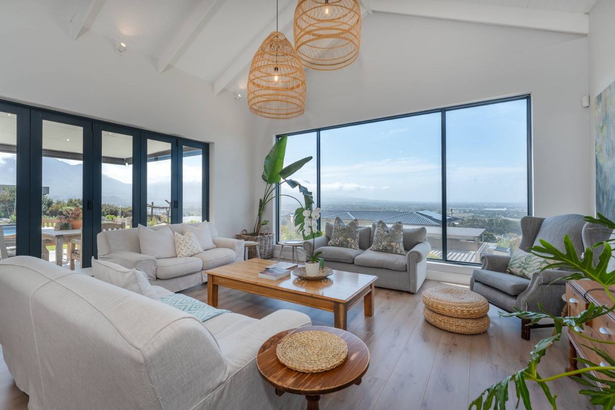 Spacious living room featuring a vaulted ceiling with exposed rafters, large floor-to-ceiling windows, and bi-fold doors opening to an outdoor area with scenic views.