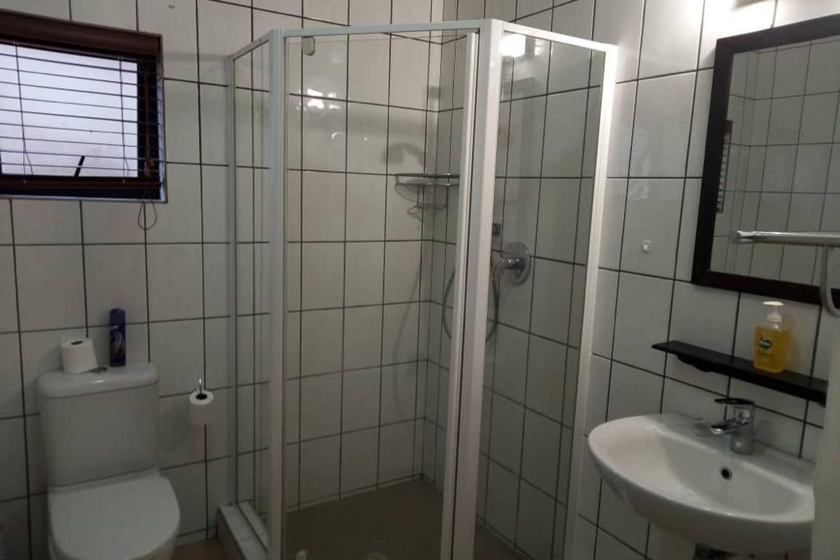 A functional bathroom featuring a corner shower enclosure, a white ceramic toilet, and a wall-mounted basin with a framed mirror.