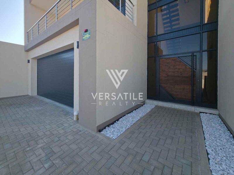 Modern front elevation featuring a double garage, paved driveway, and a striking glass-fronted entrance with balcony access above.