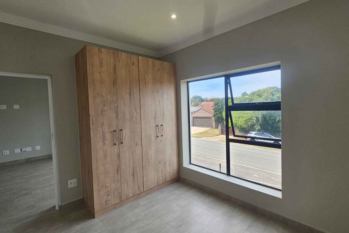 A bright bedroom featuring modern wood-finish built-in cupboards, tiled flooring, and a large window providing natural light and street views.