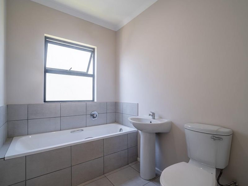 A clean and functional bathroom featuring a built-in bathtub with tiled surround, a pedestal basin, and a standard toilet.