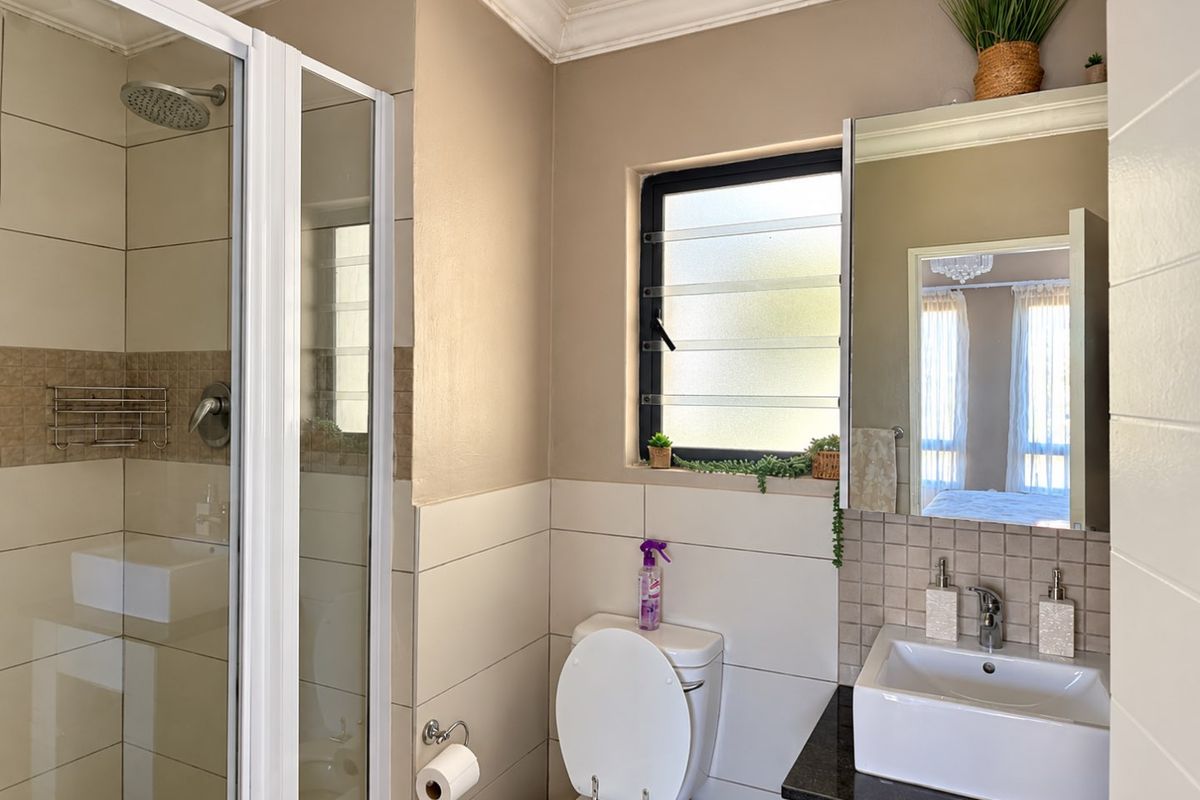 A well-maintained bathroom featuring a glass-enclosed shower, modern vanity with a granite countertop, and a louvered window for natural ventilation.
