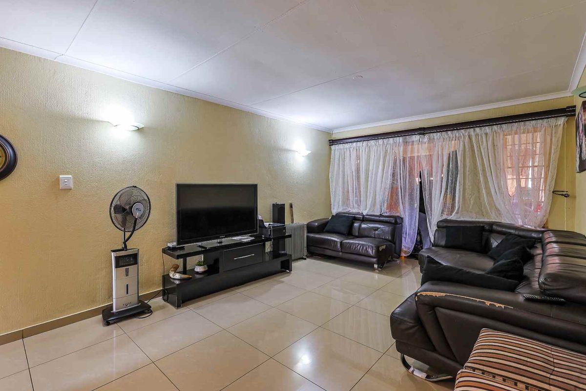A spacious living room featuring tiled flooring, wall-mounted lighting, and large windows with curtains leading to an outdoor area.