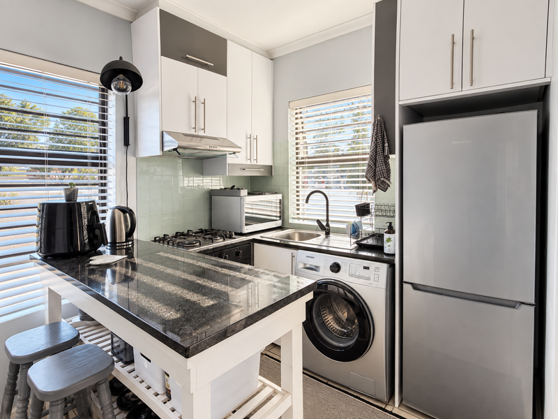 Compact modern kitchen featuring granite countertops, gas hob, extractor fan, tiled backsplash, and integrated washing machine with ample built-in cabinetry.