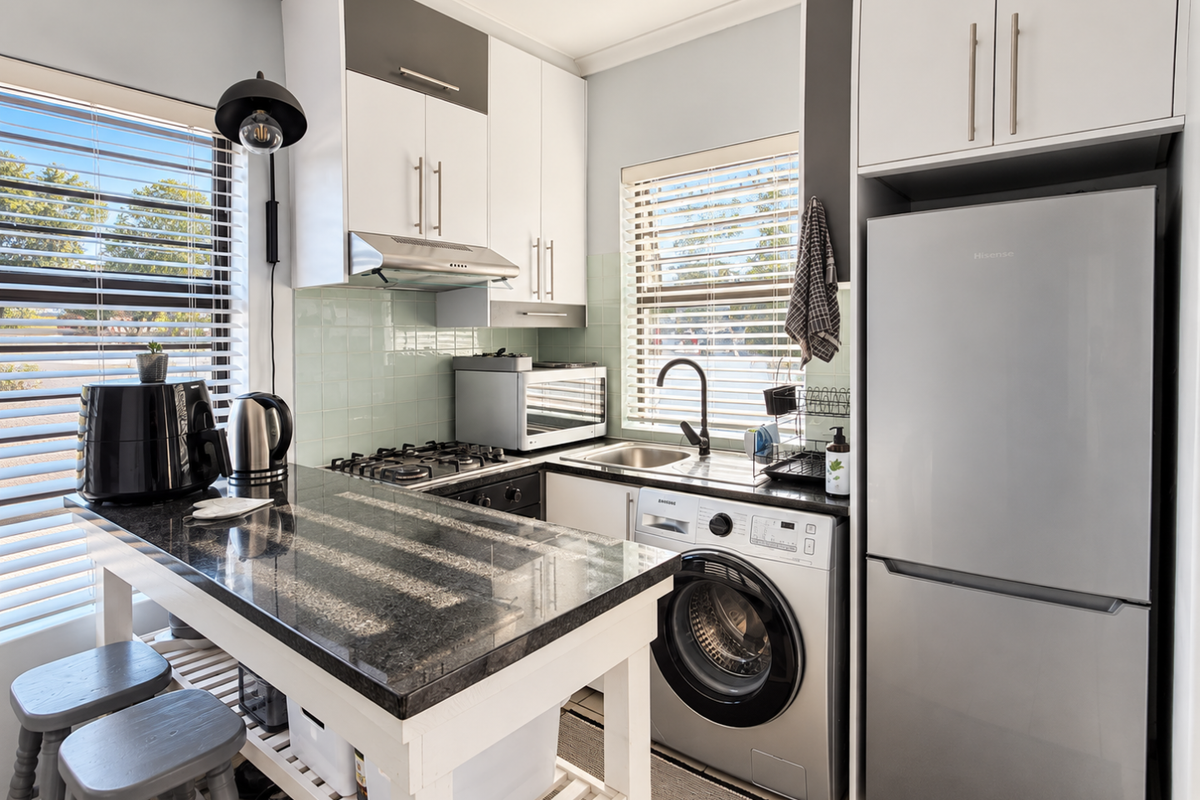 Compact modern kitchen featuring granite countertops, gas hob, extractor fan, tiled backsplash, and integrated washing machine with ample built-in cabinetry.
