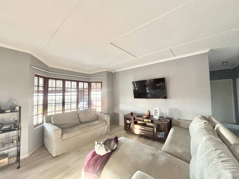A comfortable living room featuring a large bay window, neutral wall tones, and laminate flooring, providing a bright and functional space for relaxation.