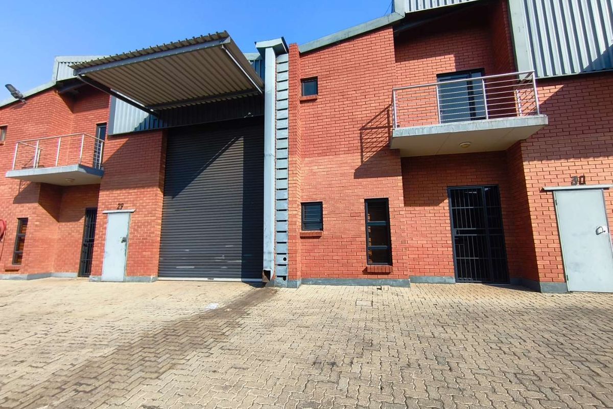 Front view of an industrial unit featuring a large roller shutter door, brick facade, and upper-level balconies with metal railings.