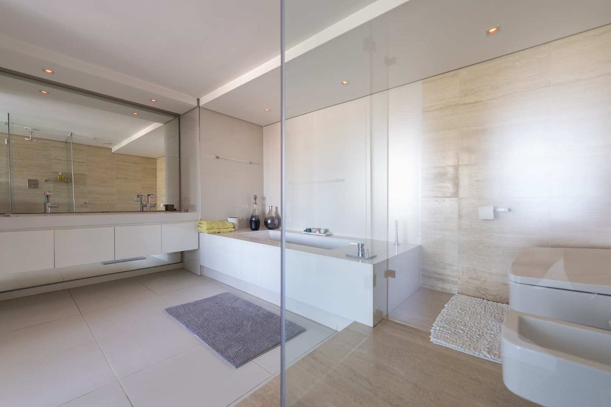 Modern luxury bathroom featuring a built-in bathtub, glass shower enclosure, wall-mounted toilet, bidet, and a sleek vanity with integrated double basins.