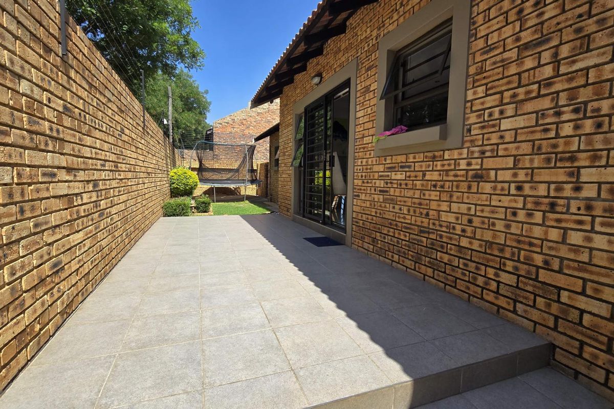 A paved rear patio area featuring face-brick walls, sliding glass doors, and a small adjacent garden space.