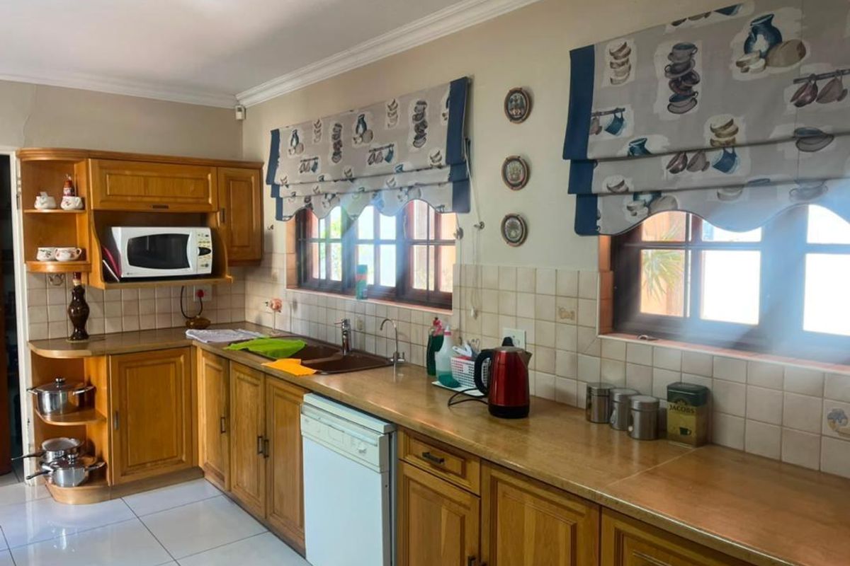 A functional kitchen featuring wooden cabinetry, tiled backsplash, and double basin sink, with natural light provided by two windows.