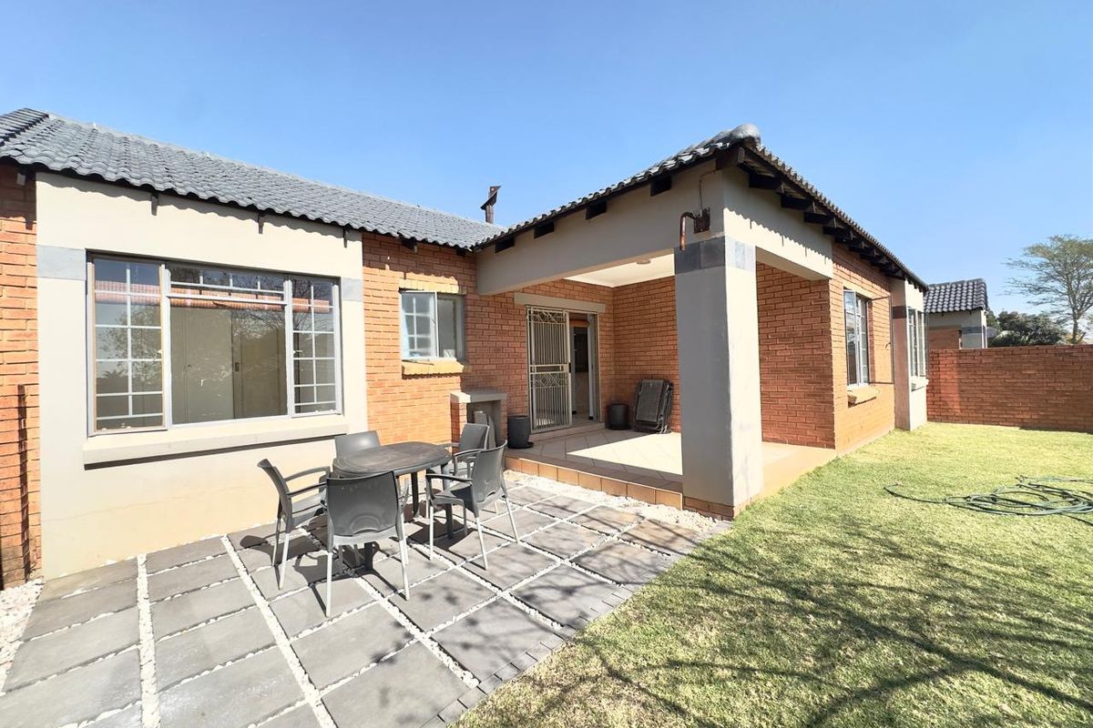 Rear view of the townhouse featuring a covered patio, paved outdoor seating area, and a well-maintained garden with brick exterior walls.