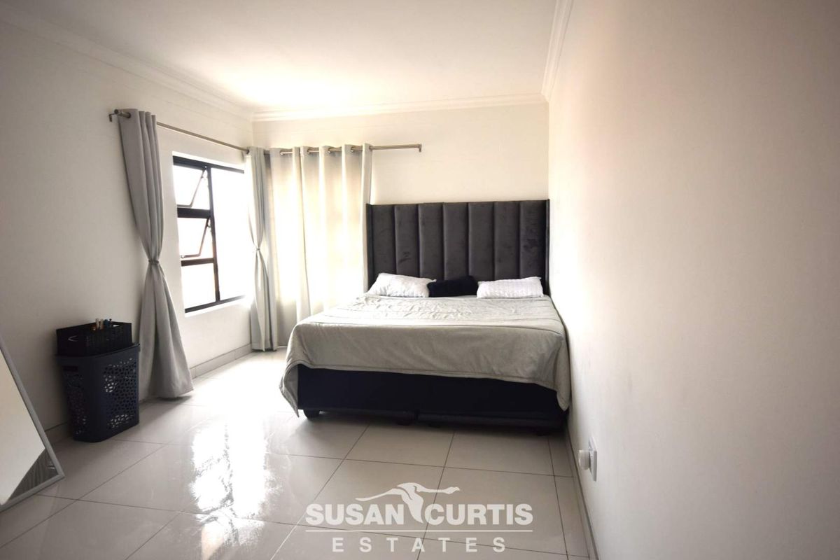 A bright bedroom featuring large format floor tiles, neutral walls, and a window with curtain tracks.