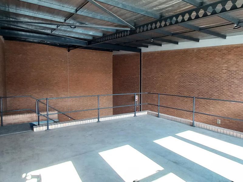 An open-plan industrial utility space featuring exposed steel roof trusses, face brick walls, and concrete flooring with a metal safety railing.