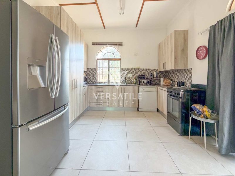 A functional kitchen featuring light wood-finish cabinetry, tiled backsplash, tiled flooring, and an arched window providing natural light.