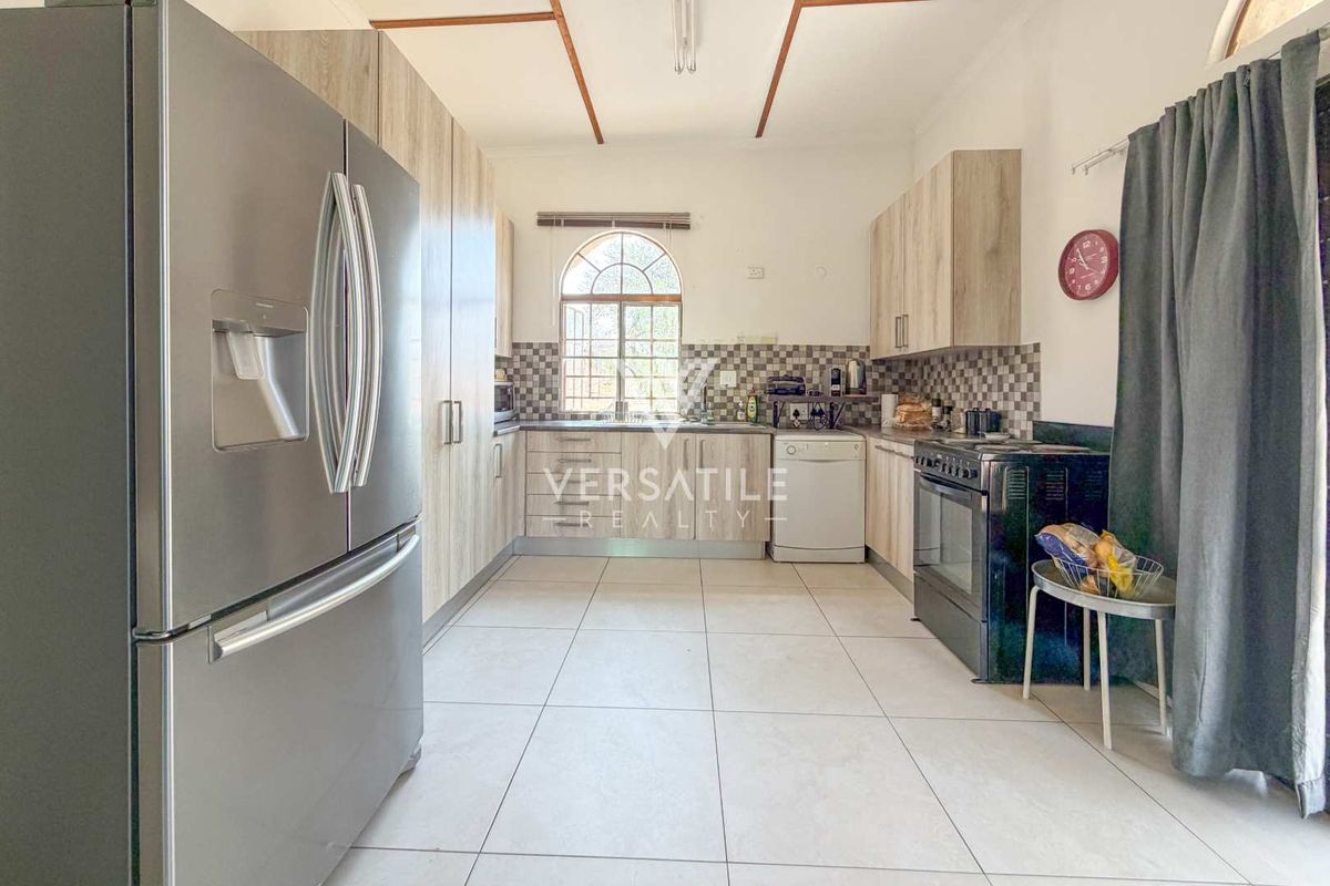 A functional kitchen featuring light wood-finish cabinetry, tiled backsplash, tiled flooring, and an arched window providing natural light.