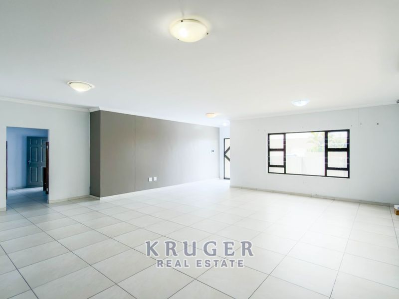 A spacious, open-plan living area featuring neutral tiled flooring, large aluminium-framed windows, and a wall-mounted air conditioning unit.