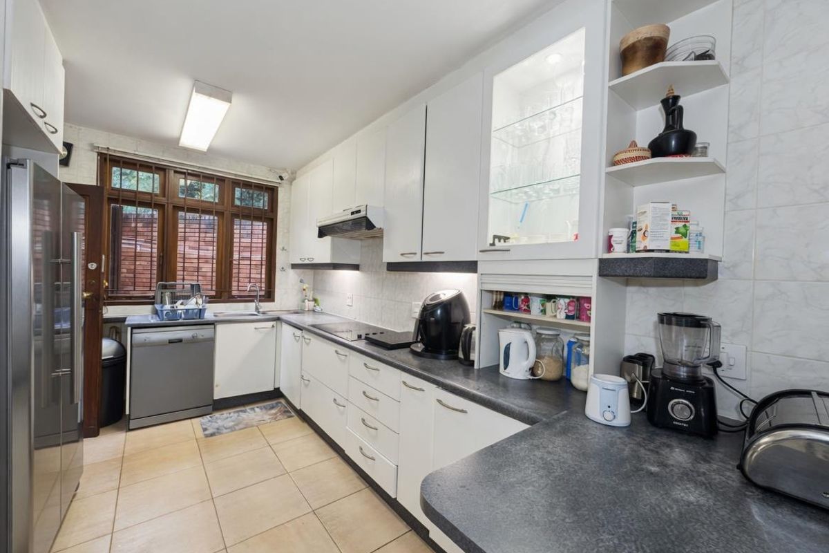 A functional kitchen featuring white cabinetry, dark laminate countertops, tiled flooring, and a glass-fronted display cabinet with integrated lighting.