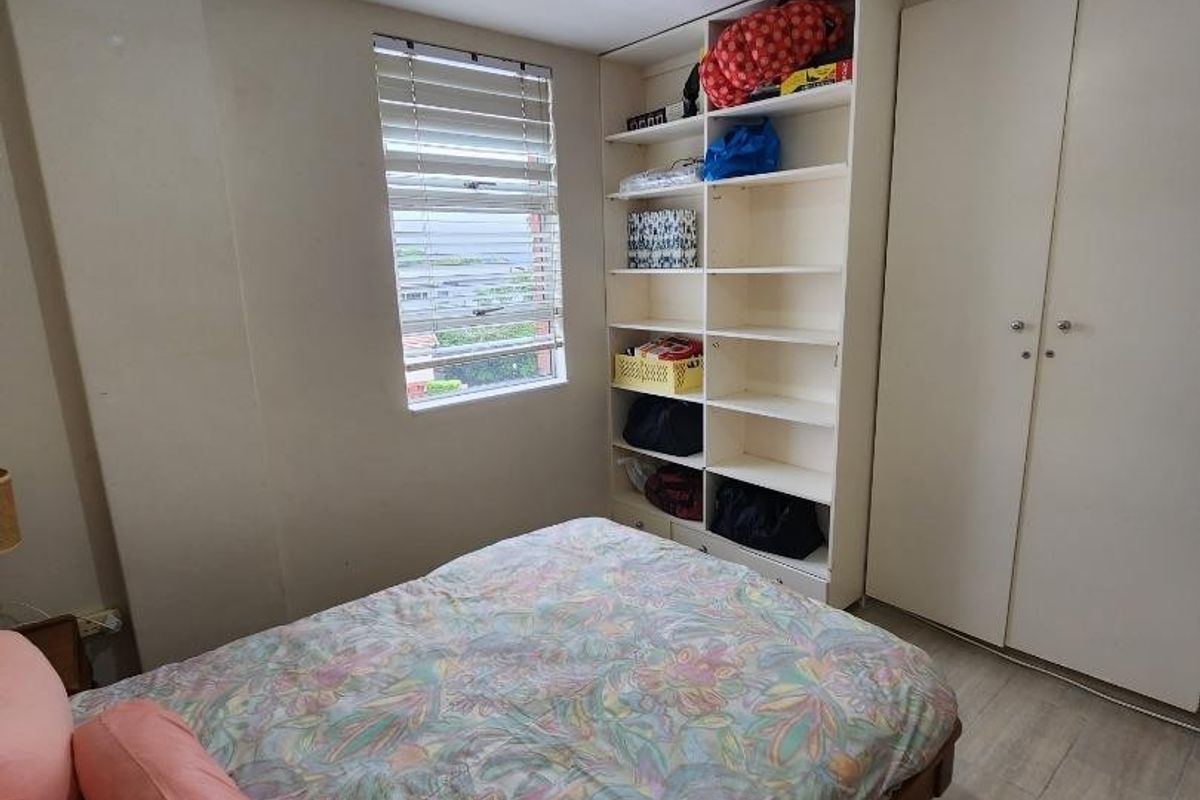 A bedroom featuring built-in wardrobes, integrated shelving, tiled flooring, and a window with venetian blinds, providing functional storage and natural light.