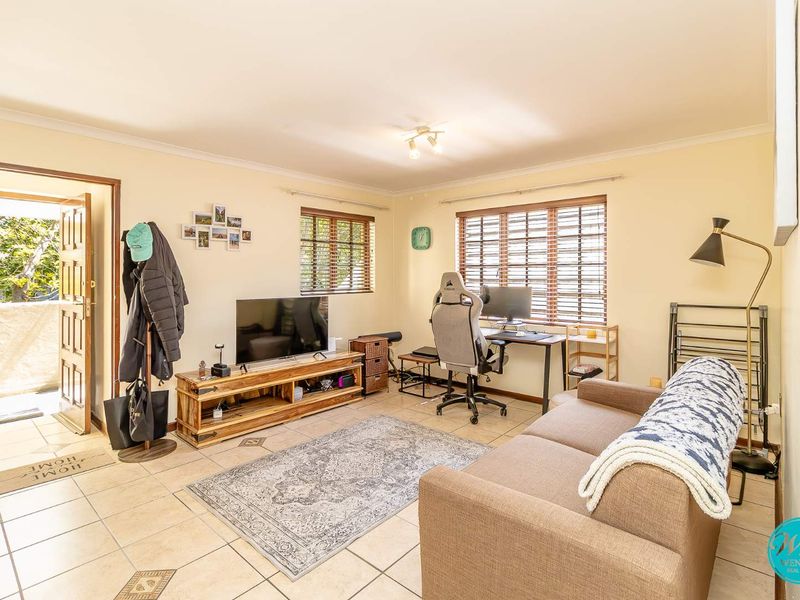 A functional living room featuring tiled flooring, coved ceiling cornices, and natural light through wooden blinds, providing a comfortable and versatile living space.