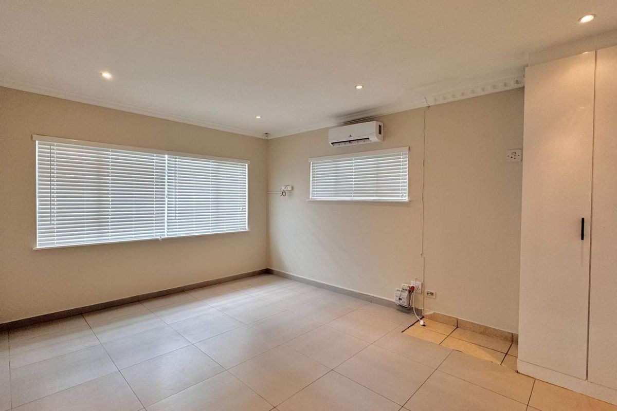 A spacious, empty bedroom featuring tiled flooring, built-in cupboards, an air conditioning unit, and recessed lighting.