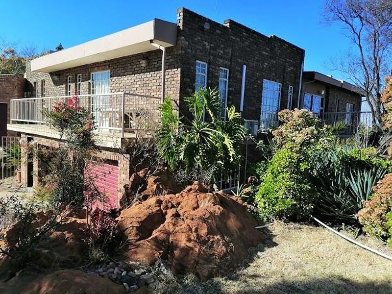 Rear exterior view of a brick house featuring a balcony, metal railings, and a lower-level garage, set against a natural rocky landscape.