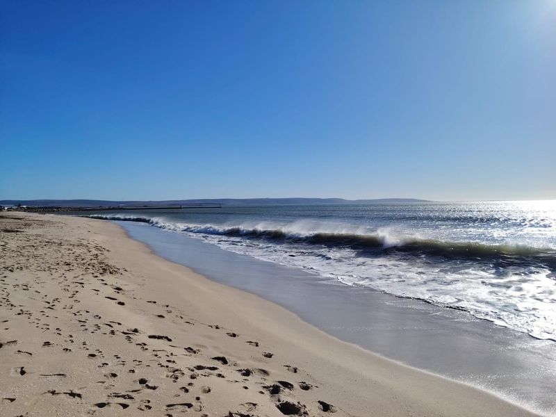 A scenic view of the sandy beach and ocean waves under a clear blue sky.