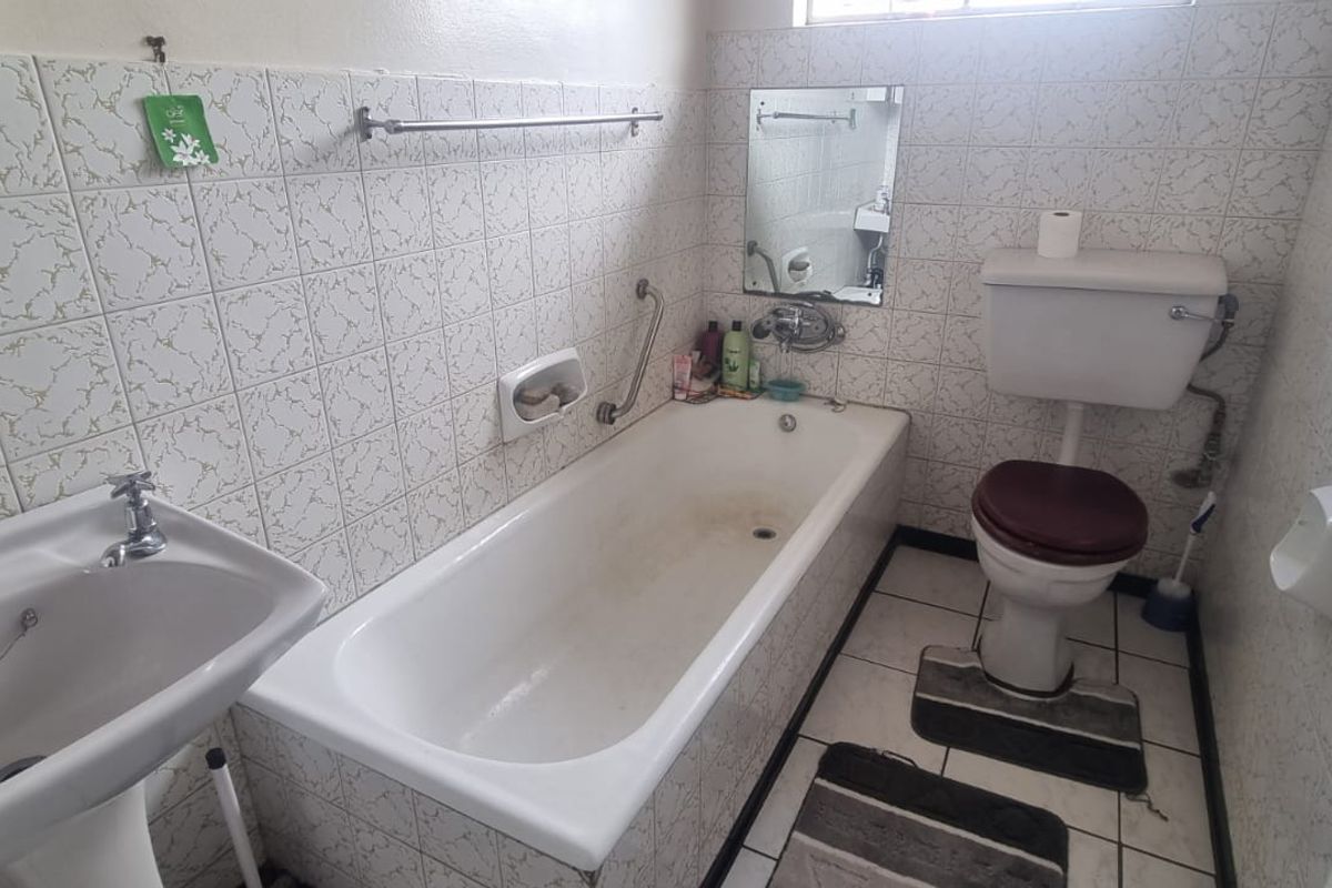 A dated bathroom featuring a standard bathtub, pedestal basin, and toilet with original wall tiling and ceramic floor finishes.